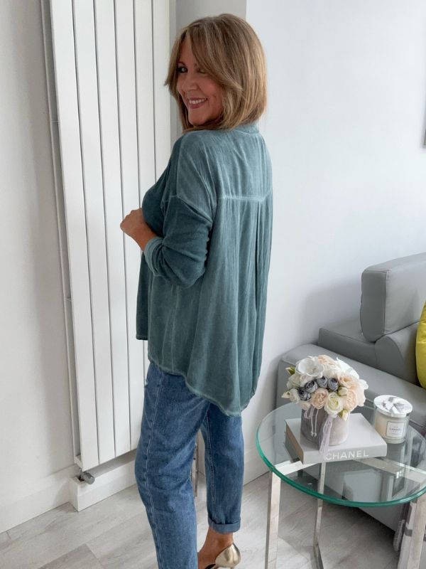 Woman wearing a vintage rose two-tone blouse with button details, paired with blue jeans and gold pointed flats, standing indoors by a round glass table and a flower arrangement.