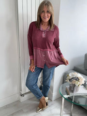 Woman wearing a vintage rose two-tone blouse with button details, paired with blue jeans and gold pointed flats, standing indoors by a round glass table and a flower arrangement.
