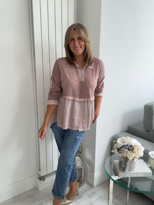 Woman wearing a vintage rose two-tone blouse with button details, paired with blue jeans and gold pointed flats, standing indoors by a round glass table and a flower arrangement.