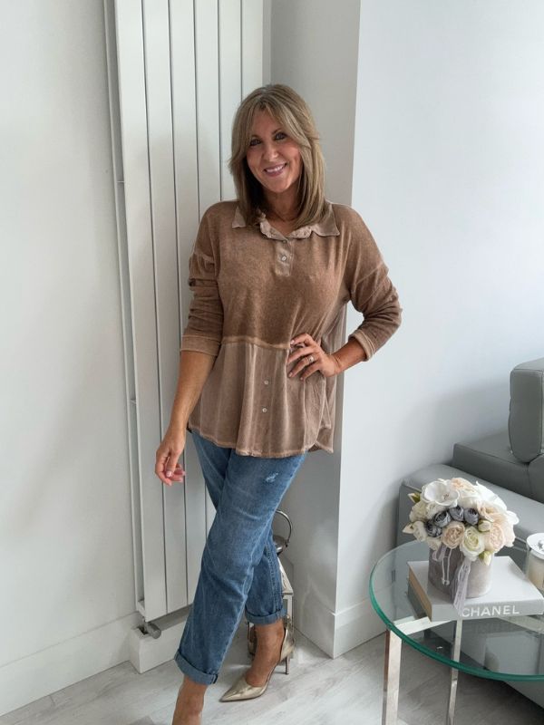 Woman wearing a vintage rose two-tone blouse with button details, paired with blue jeans and gold pointed flats, standing indoors by a round glass table and a flower arrangement.