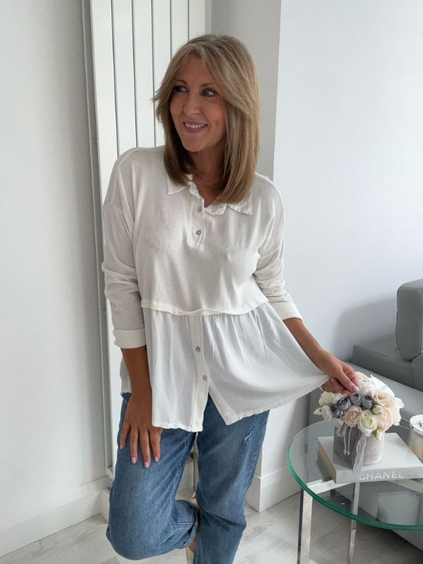 Woman wearing a vintage rose two-tone blouse with button details, paired with blue jeans and gold pointed flats, standing indoors by a round glass table and a flower arrangement.