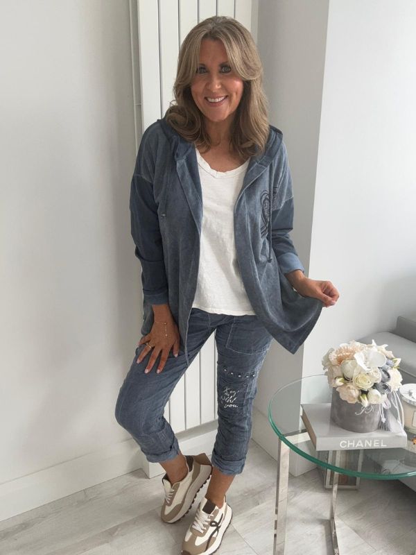 Woman wearing a velour zip-up hoodie jacket with pockets and embroidered detail, styled with matching joggers and a white top.