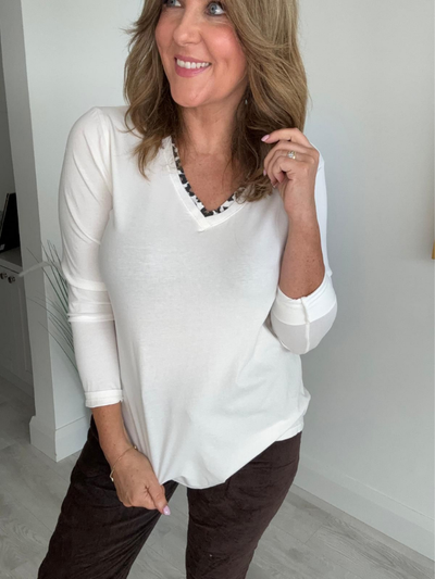 Smiling individual posing indoors, wearing a long-sleeve top and pants