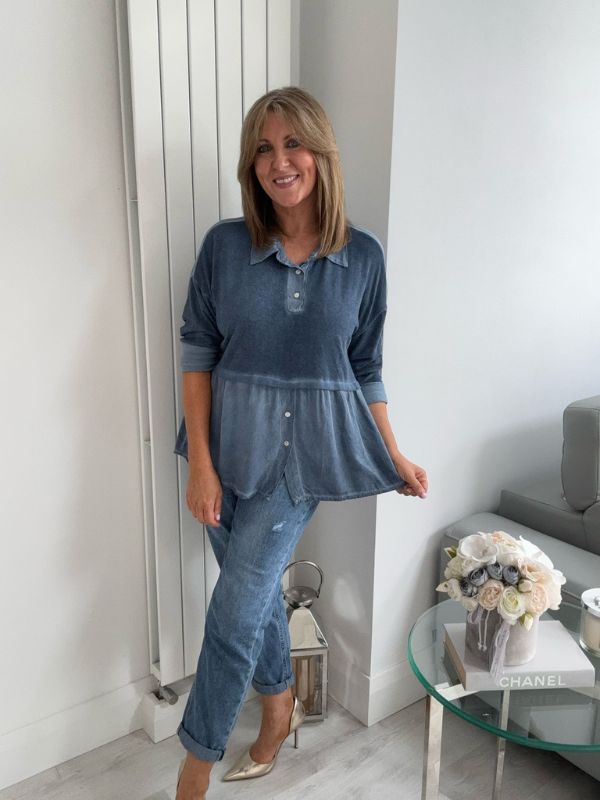 Woman wearing a vintage rose two-tone blouse with button details, paired with blue jeans and gold pointed flats, standing indoors by a round glass table and a flower arrangement.