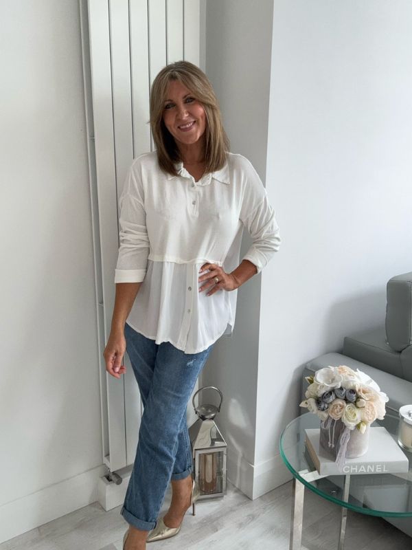 Woman wearing a vintage rose two-tone blouse with button details, paired with blue jeans and gold pointed flats, standing indoors by a round glass table and a flower arrangement.