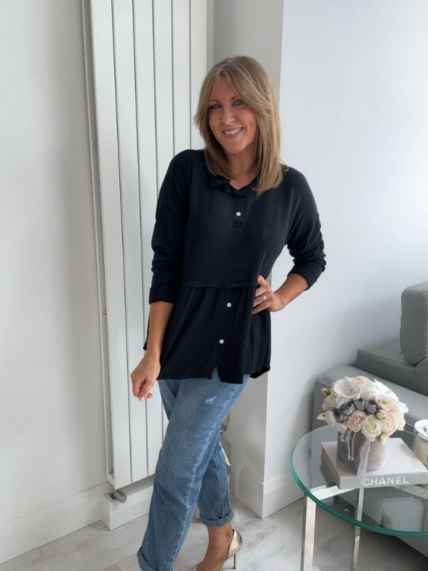 Woman wearing a vintage rose two-tone blouse with button details, paired with blue jeans and gold pointed flats, standing indoors by a round glass table and a flower arrangement.