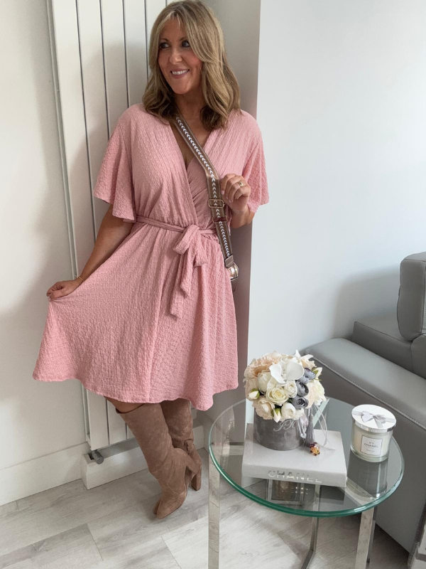 Woman in a pink dress standing in a room with a glass table and flowers.