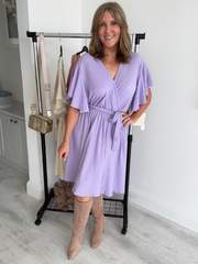 Woman wearing a purple dress and brown knee-high boots in a room with a white wall and wooden floor.