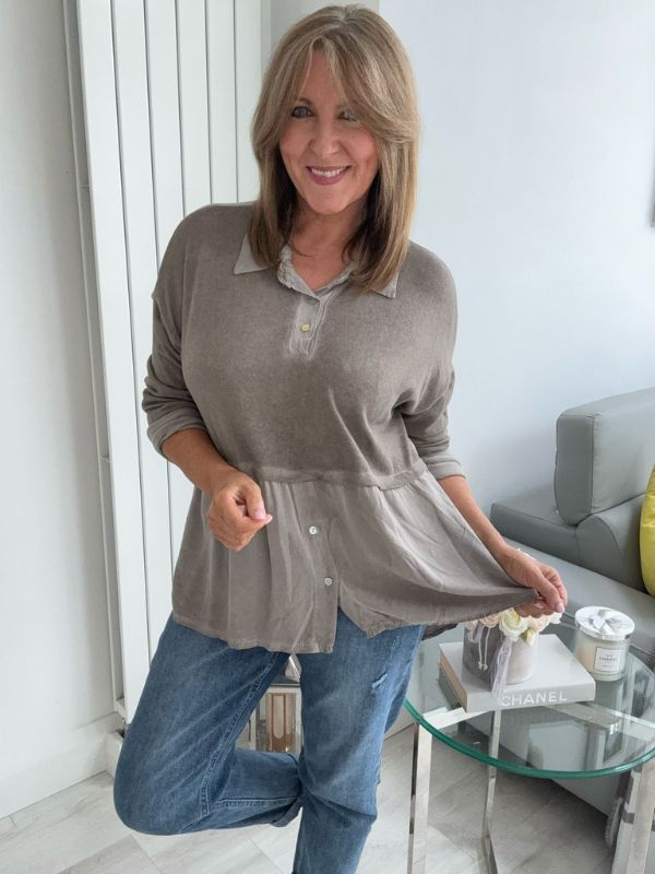 Woman wearing a vintage rose two-tone blouse with button details, paired with blue jeans and gold pointed flats, standing indoors by a round glass table and a flower arrangement.