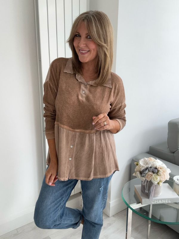Woman wearing a vintage rose two-tone blouse with button details, paired with blue jeans and gold pointed flats, standing indoors by a round glass table and a flower arrangement.