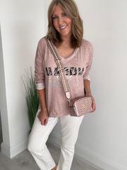 Woman wearing a pink graphic t-shirt and white pants, holding a matching handbag.