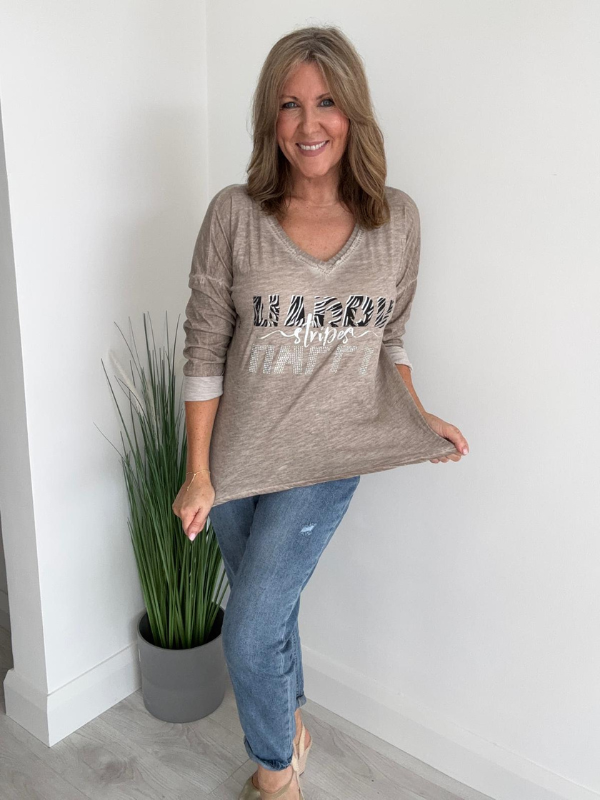 Woman wearing a brown long-sleeve shirt with a graphic design, standing indoors next to a plant.