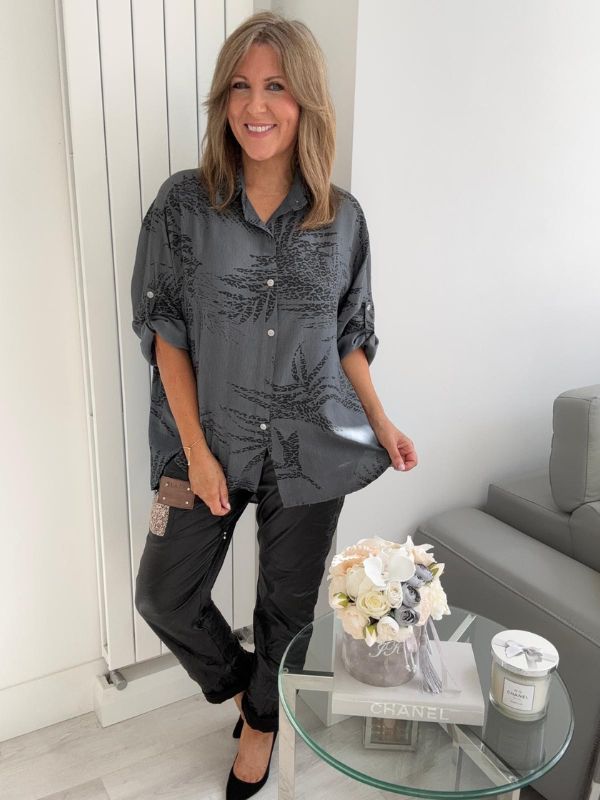 Woman wearing a printed button-down shirt with roll-up sleeves and black pants.