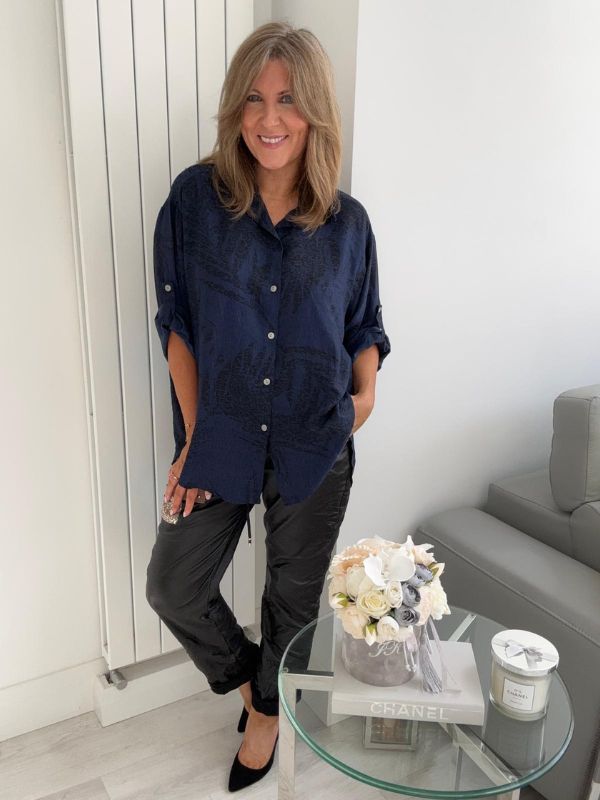 Woman wearing a printed button-down shirt with roll-up sleeves and black pants.