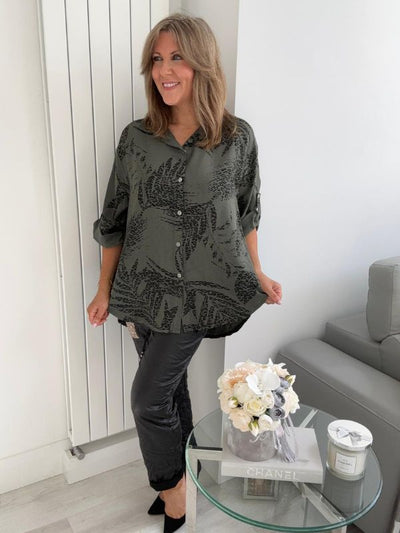 Woman wearing a printed button-down shirt with roll-up sleeves and black pants.