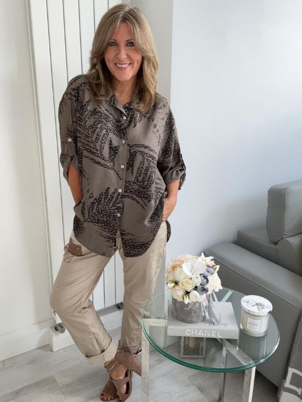 Woman wearing a printed button-down shirt with roll-up sleeves and black pants.