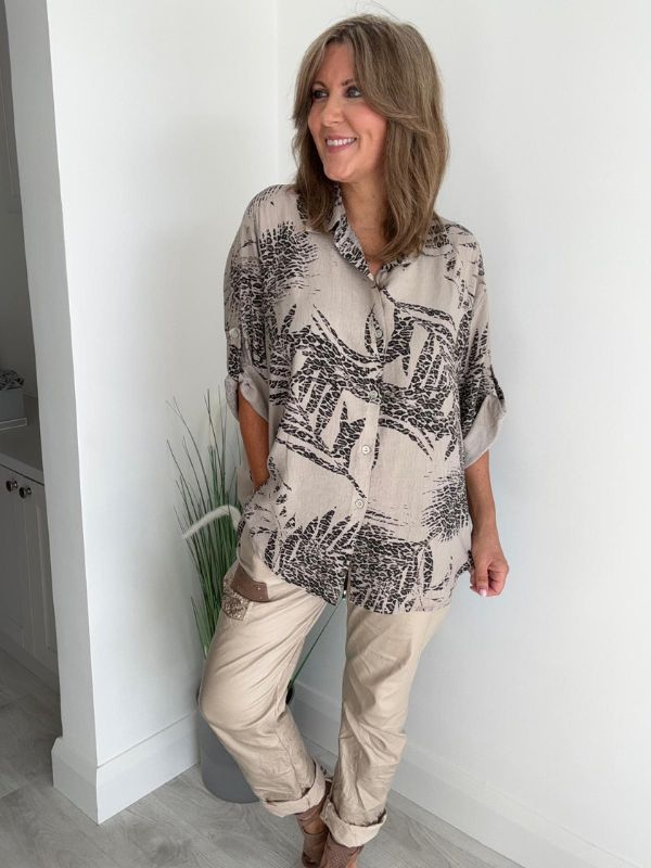 Woman wearing a printed button-down shirt with roll-up sleeves and black pants.