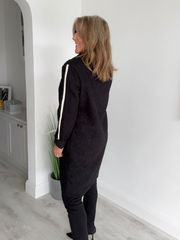 Woman wearing a black outfit with white stripes standing in a room with a white wall and gray floor.