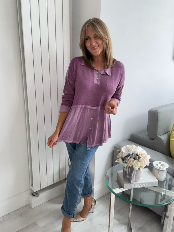 Woman wearing a vintage rose two-tone blouse with button details, paired with blue jeans and gold pointed flats, standing indoors by a round glass table and a flower arrangement.