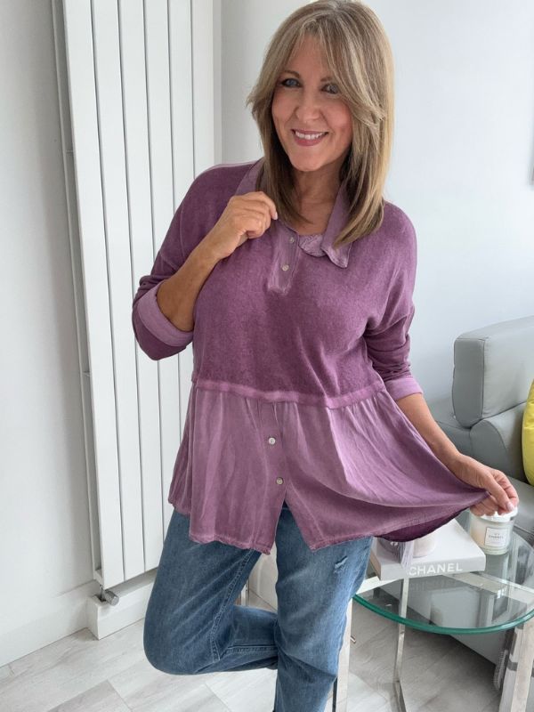 Woman wearing a vintage rose two-tone blouse with button details, paired with blue jeans and gold pointed flats, standing indoors by a round glass table and a flower arrangement.
