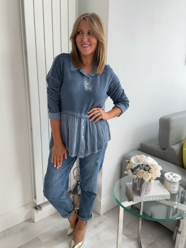Woman wearing a vintage rose two-tone blouse with button details, paired with blue jeans and gold pointed flats, standing indoors by a round glass table and a flower arrangement.