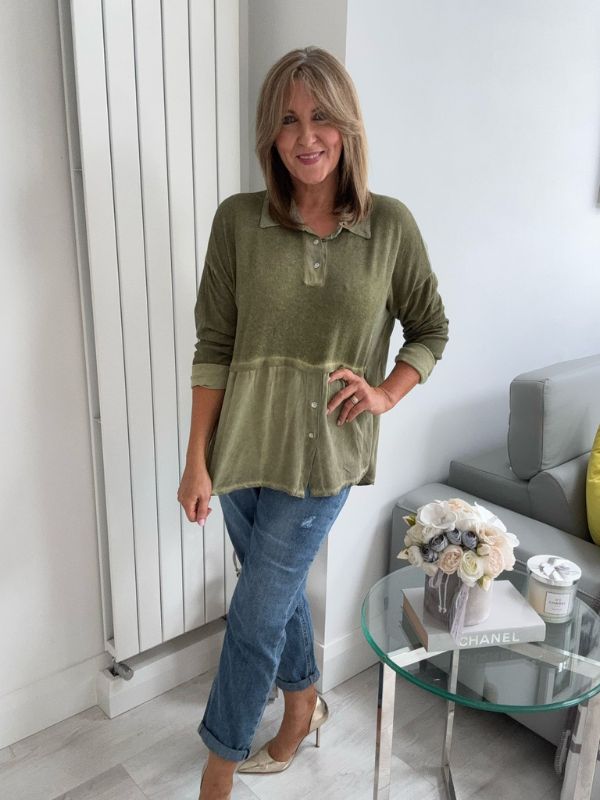 Woman wearing a vintage rose two-tone blouse with button details, paired with blue jeans and gold pointed flats, standing indoors by a round glass table and a flower arrangement.
