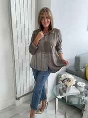 Woman wearing a vintage rose two-tone blouse with button details, paired with blue jeans and gold pointed flats, standing indoors by a round glass table and a flower arrangement.