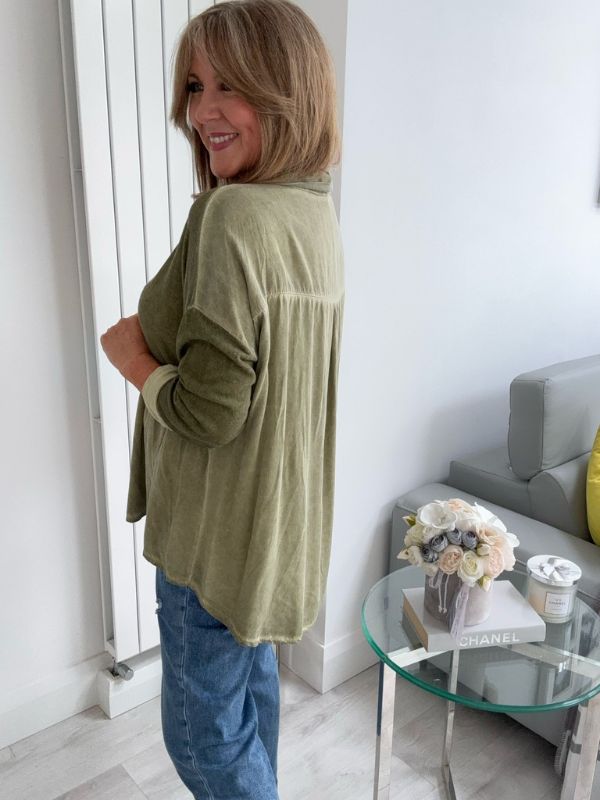 Woman wearing a vintage rose two-tone blouse with button details, paired with blue jeans and gold pointed flats, standing indoors by a round glass table and a flower arrangement.