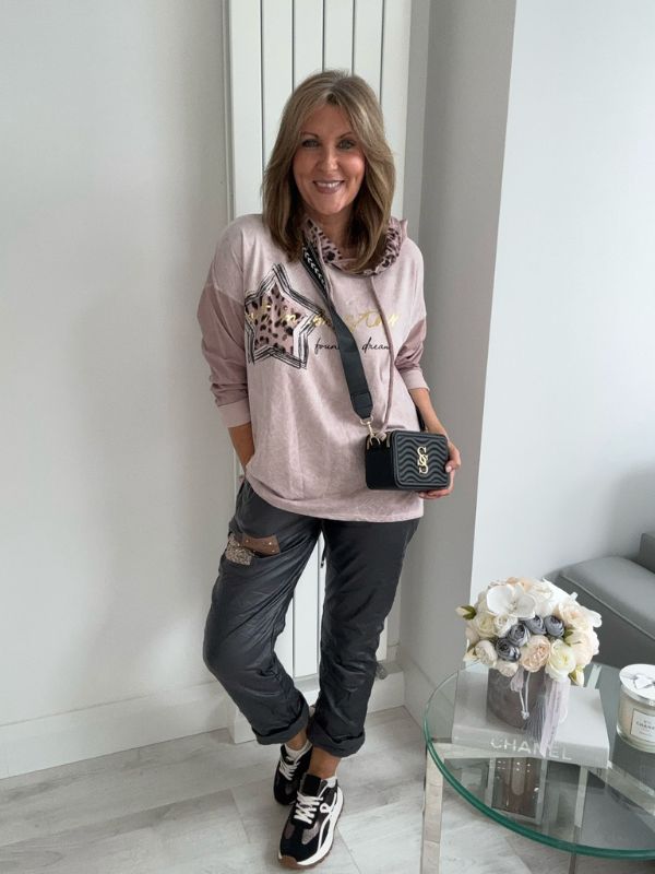 Woman in a pink sweatshirt with star designs and gray pants standing in a modern interior setting.