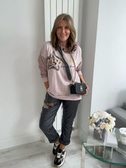 Woman in a pink sweatshirt with star designs and gray pants standing in a modern interior setting.