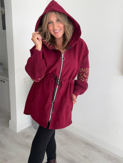 Woman wearing a burgundy hooded coat with leopard print sleeves indoors.