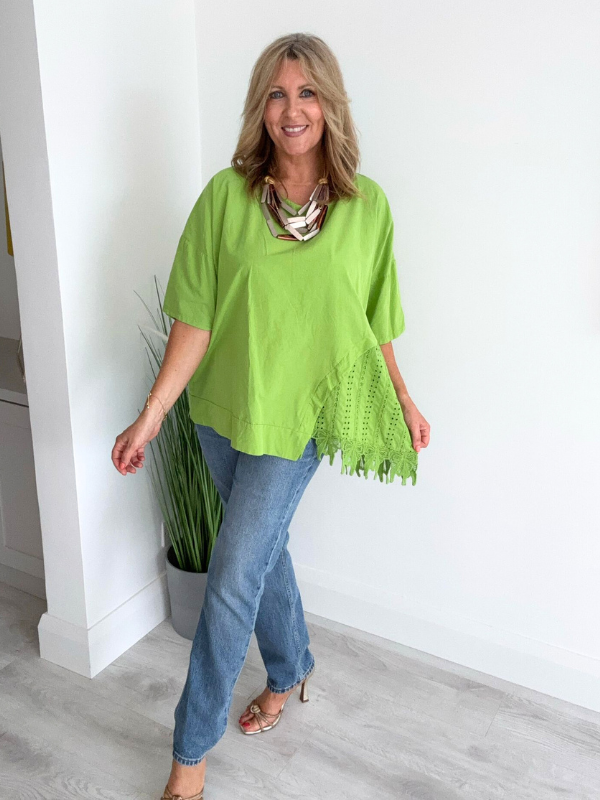 Woman wearing an asymmetric cotton top with lace side detail, styled with jeans and heels