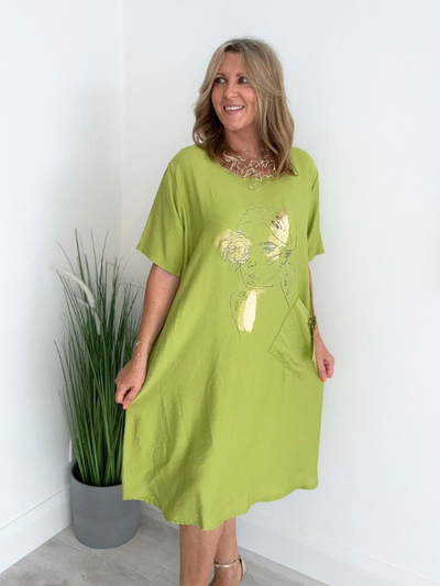 Model wearing a Boho Chic oversized tunic dress featuring a gold foil abstract face print, short sleeves, and a front pocket with buckle detail – available in khaki, lime, grey, pink, off-white, blush, and sky blue, fits sizes 8–18.