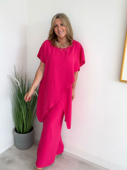 Model wearing an asymmetric co-ord set featuring a short-sleeve top with an uneven hem and matching wide-leg trousers, available in hot pink and blush, designed to fit UK sizes 8–18