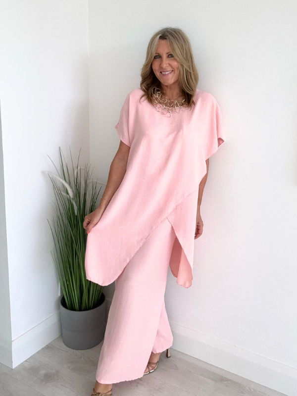 Model wearing an asymmetric co-ord set featuring a short-sleeve top with an uneven hem and matching wide-leg trousers, available in hot pink and blush, designed to fit UK sizes 8–18