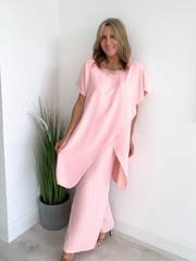 Model wearing an asymmetric co-ord set featuring a short-sleeve top with an uneven hem and matching wide-leg trousers, available in hot pink and blush, designed to fit UK sizes 8–18