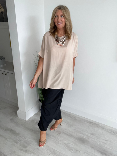 Model wearing a beige oversized viscose top with short sleeves and a relaxed draped fit, styled for a minimalist and elegant everyday look.
