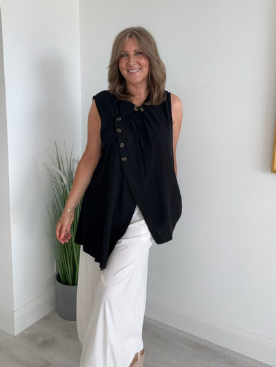 Model wearing asymmetric buttoned sleeveless vest top – relaxed fit and draped silhouette