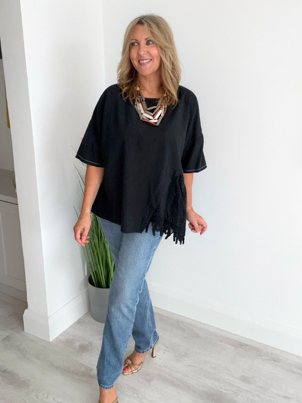 Woman wearing an asymmetric cotton top with lace side detail, styled with jeans and heels