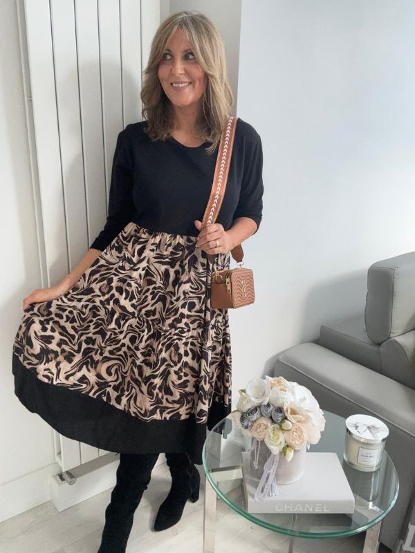 Woman wearing a black top and leopard print skirt in a living room setting.