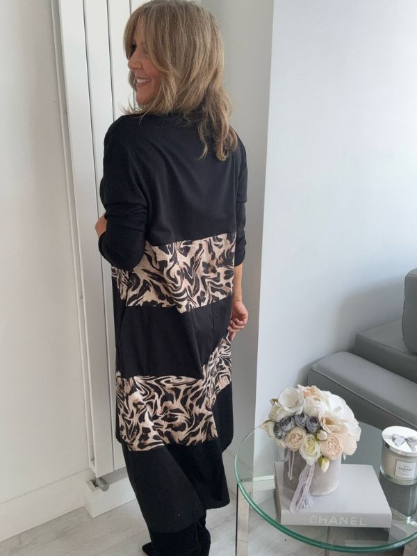 Woman wearing a black and animal print dress standing in front of a mirror.