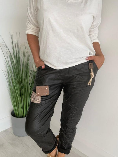 Women’s leatherette joggers in faux leather with soft fleece lining, elastic waistband, adjustable drawstring, side pockets, and patch detail. 