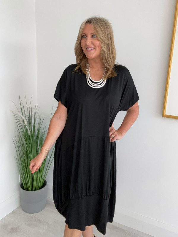 Model wearing a relaxed fit tunic dress with an asymmetric tiered hem, short sleeves, and round neckline, styled for casual comfort and everyday elegance
