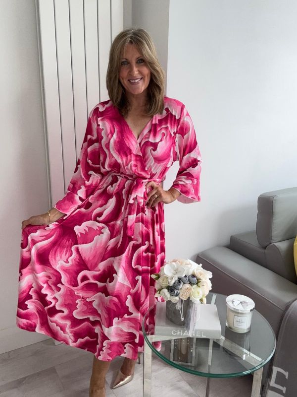Woman wearing a bold swirl print wrap midi dress with long sleeves and a waist tie, standing in a modern living space.