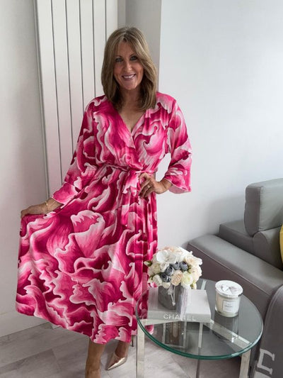 Woman wearing a bold swirl print wrap midi dress with long sleeves and a waist tie, standing in a modern living space.