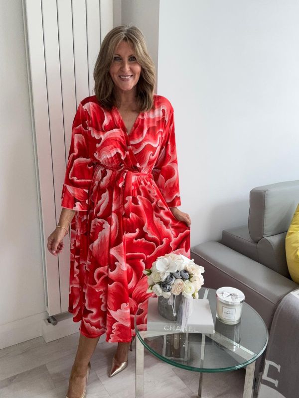 Woman wearing a bold swirl print wrap midi dress with long sleeves and a waist tie, standing in a modern living space.