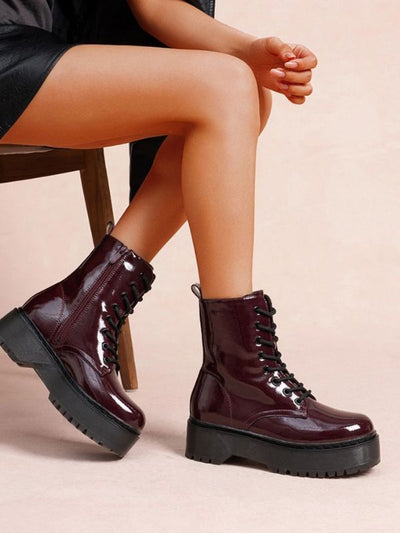 Burgundy patent platform combat boots with a glossy finish, chunky black sole, lace-up front, and side zipper, designed for bold and stylish everyday wear.
