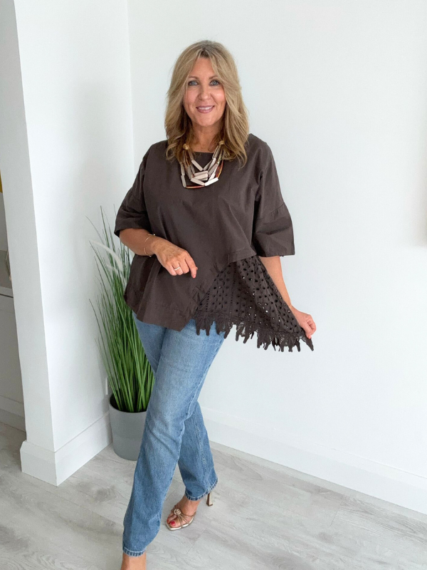 Woman wearing an asymmetric cotton top with lace side detail, styled with jeans and heels