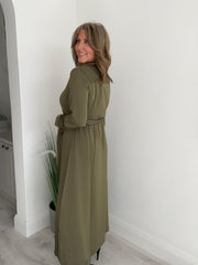 Woman wearing a khaki green button-down belted maxi shirt dress with long sleeves.