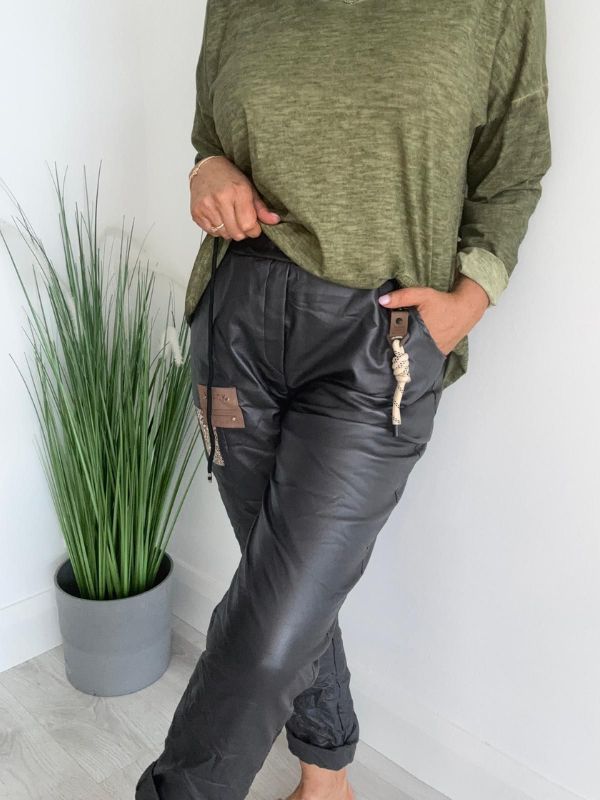 Women’s leatherette joggers in faux leather with soft fleece lining, elastic waistband, adjustable drawstring, side pockets, and patch detail. 